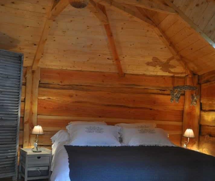 Chalet en bois chaleureux avec lit douillet et plafond en poutres apparentes.