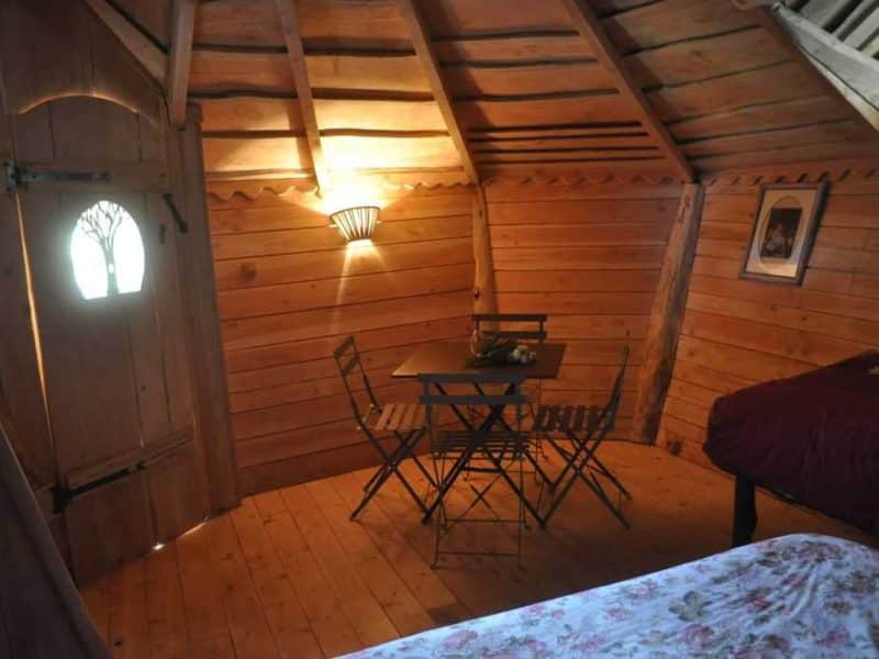 Cabane en bois chaleureuse avec table et chaises, ambiance cosy et lumineuse.