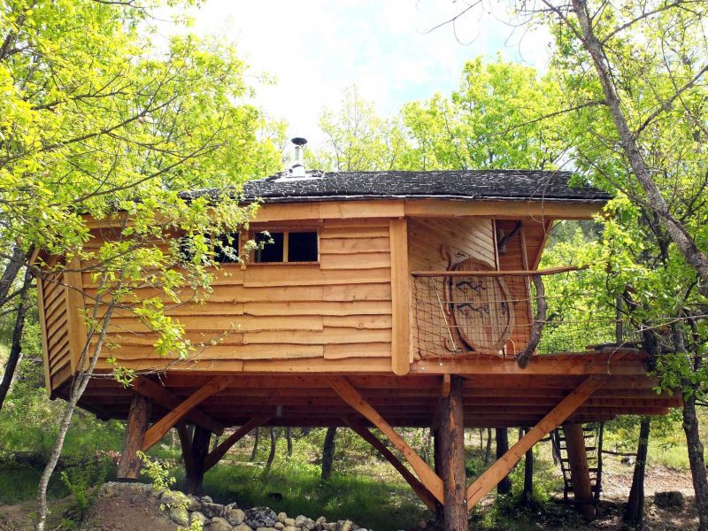 Cabane perchée en bois, entourée darbres verdoyants en Auvergne-Rhône-Alpes.