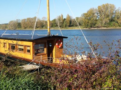 Hébergement insolite : une péniche en bois amarrée au bord de la rivière, entourée de verdure.