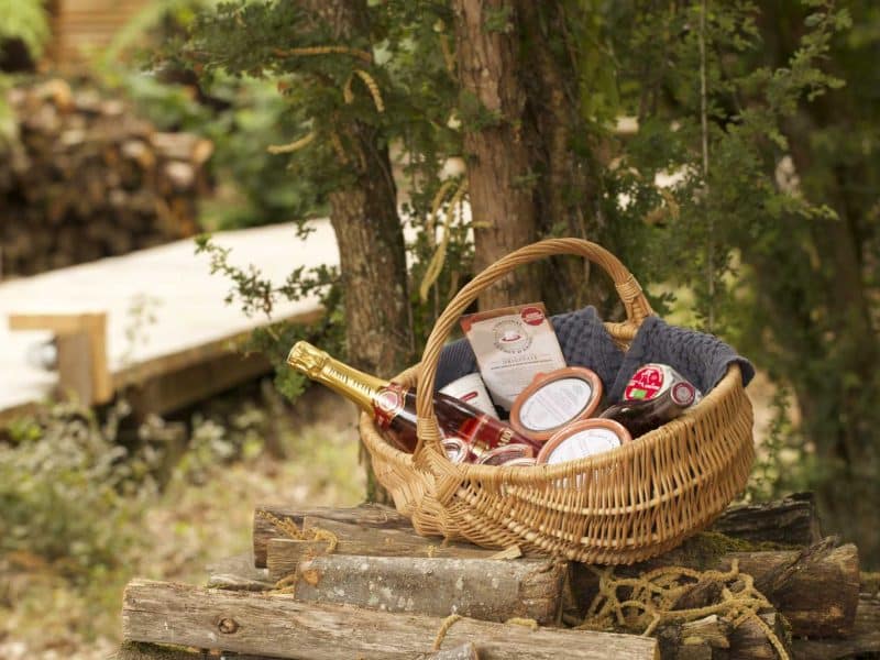 Panier en osier rempli de produits locaux, à côté dun hébergement en pleine nature.