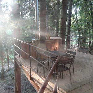 Cabane perchée en Aquitaine avec terrasse en bois et jacuzzi entouré darbres.