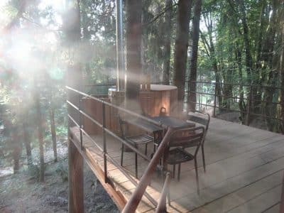 Cabane perchée en Aquitaine avec terrasse en bois et jacuzzi entouré darbres.