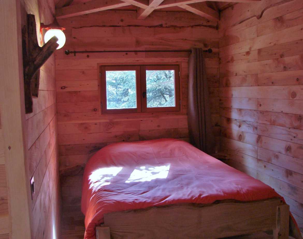 Cabane en bois dans le Languedoc-Roussillon, lit simple avec draps orange et lumière douce.