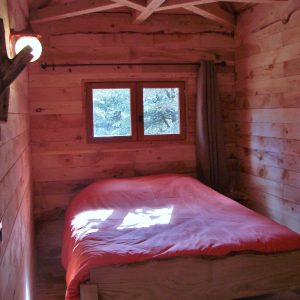 Cabane en bois dans le Languedoc-Roussillon, lit simple avec draps orange et lumière douce.