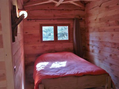 Cabane en bois dans le Languedoc-Roussillon, lit simple avec draps orange et lumière douce.