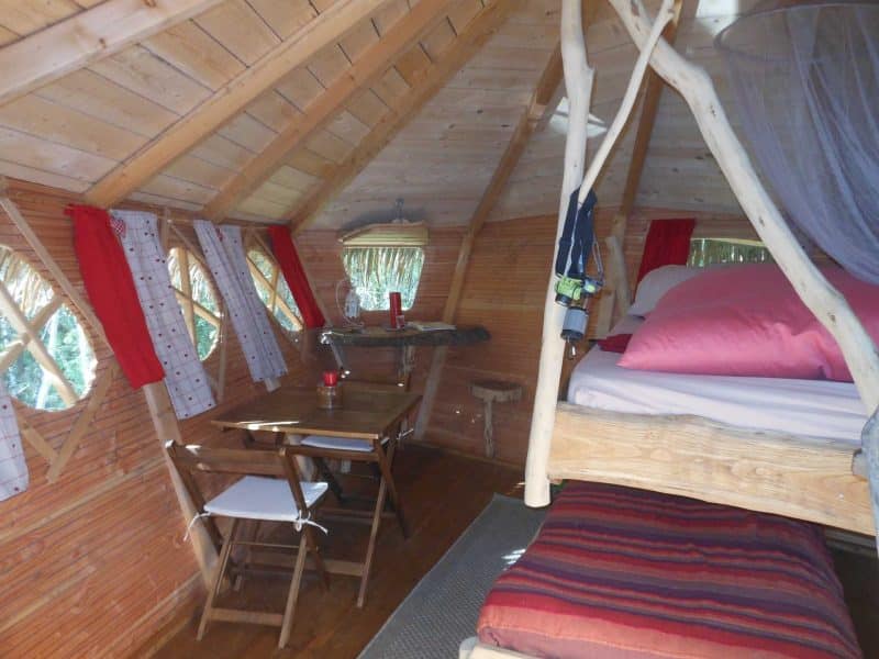 Cabane en bois avec lit douillet et table en bois, ambiance chaleureuse et naturelle.