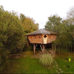Cabane perchée en bois au cœur de la nature bretonne, entourée darbres.