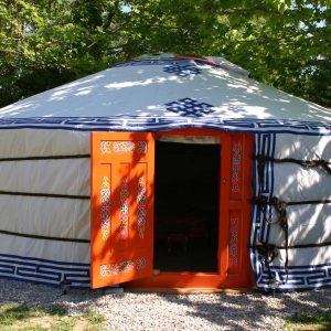 Yourte colorée avec porte orange, nichée dans la verdure de Provence-Alpes-Côte dAzur.