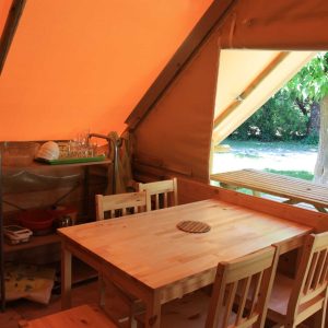 Tente lodge en Provence-Alpes-Côte dAzur, avec table en bois et vue sur la verdure.