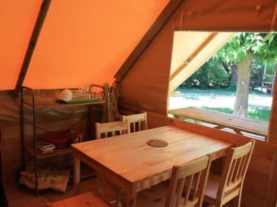 Tente lodge en Provence-Alpes-Côte dAzur, avec table en bois et vue sur la verdure.