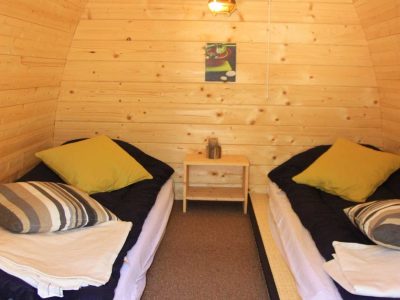 Hébergement insolite en forme de cabane en bois, avec lits jumeaux et décoration chaleureuse.