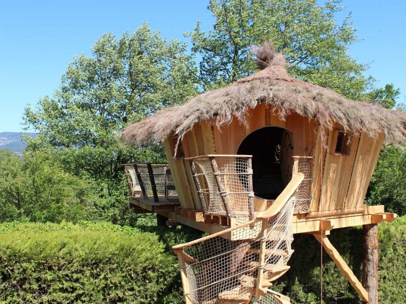 Cabane perchée en bois avec toit en chaume, entourée de verdure en Provence.
