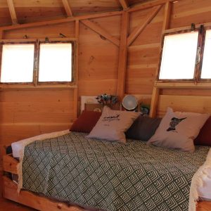 Hébergement insolite en bois avec un lit douillet et des fenêtres lumineuses.