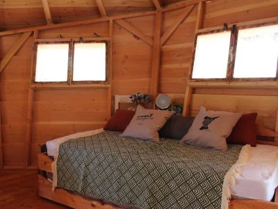 Hébergement insolite en bois avec un lit douillet et des fenêtres lumineuses.