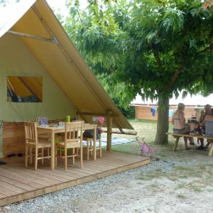 Tente safari spacieuse sous les arbres, avec une terrasse en bois et une table.