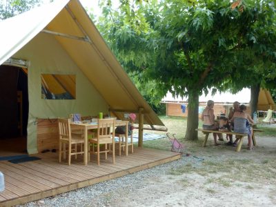 Tente safari spacieuse sous les arbres, avec une terrasse en bois et une table.