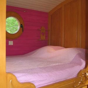 Chambre en bois avec lit douillet et mur rose, hébergement insolite en Auvergne-Rhône-Alpes.