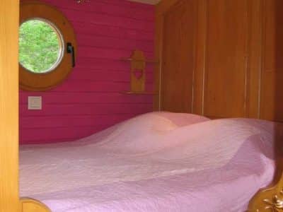 Chambre en bois avec lit douillet et mur rose, hébergement insolite en Auvergne-Rhône-Alpes.