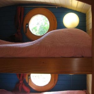 Chambre en cabane avec lits superposés et fenêtres rondes, ambiance chaleureuse.