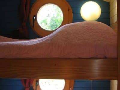 Chambre en cabane avec lits superposés et fenêtres rondes, ambiance chaleureuse.