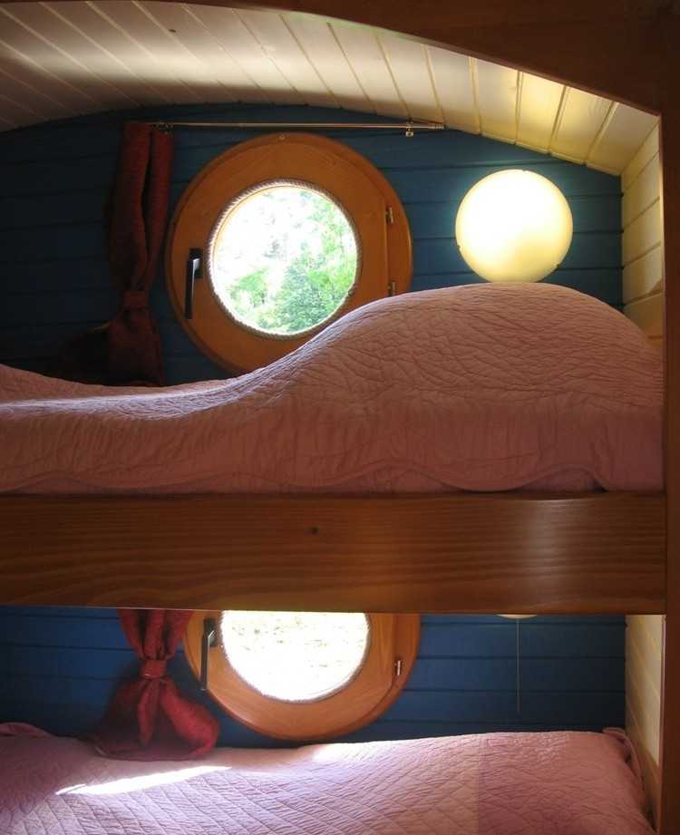 Chambre en cabane avec lits superposés et fenêtres rondes, ambiance chaleureuse.