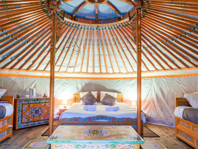 Yourte spacieuse avec un lit double et des décorations colorées en bois.