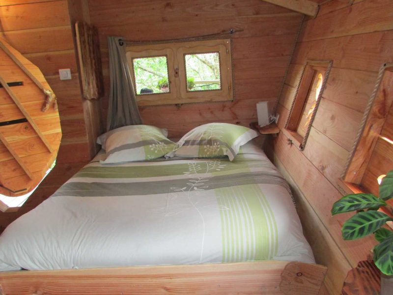 Cabane en bois avec lit douillet et fenêtres offrant une vue sur la nature.