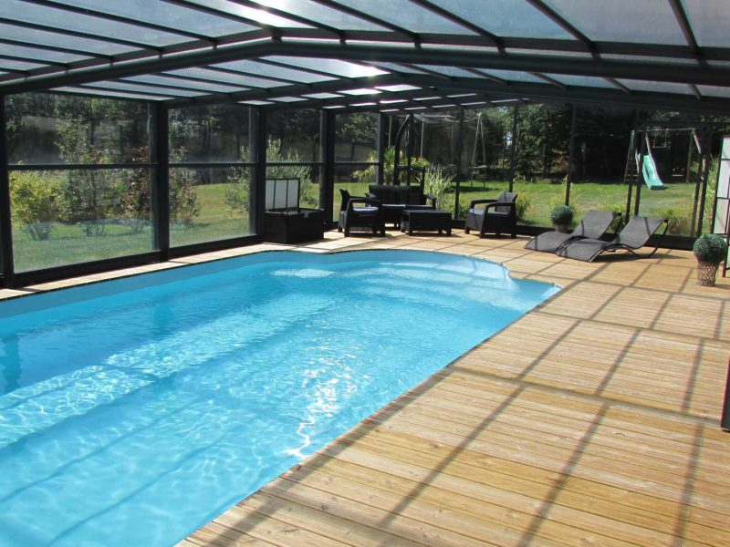 Villa moderne avec piscine intérieure, entourée de verdure et de chaises longues confortables.