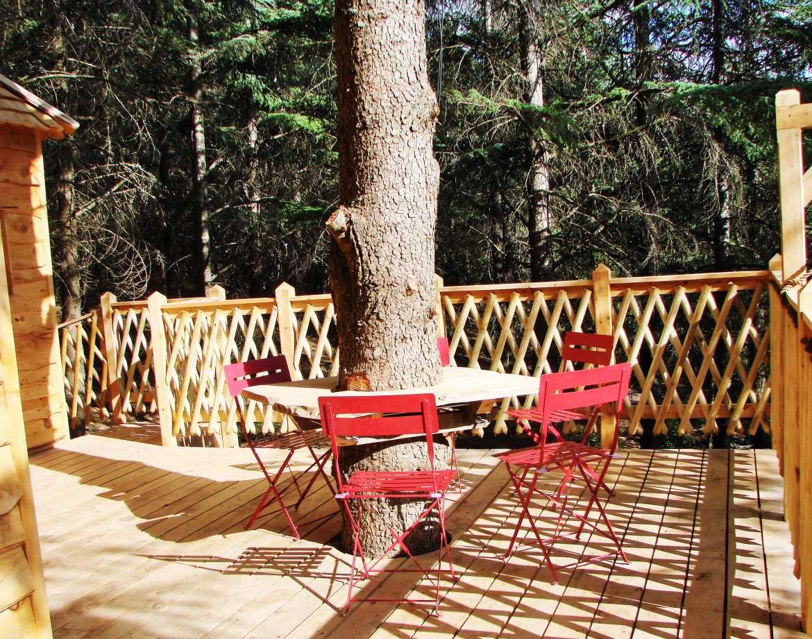 Cabane perchée en bois avec terrasse en bois et table ronde entourée darbres.