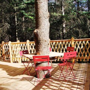 Cabane perchée en bois avec terrasse en bois et table ronde entourée darbres.