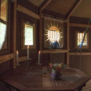 Cabane perchée en Auvergne, avec une table en bois et des fenêtres lumineuses.