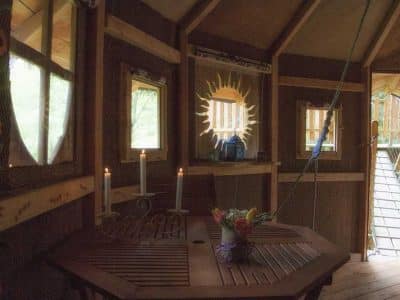 Cabane perchée en Auvergne, avec une table en bois et des fenêtres lumineuses.