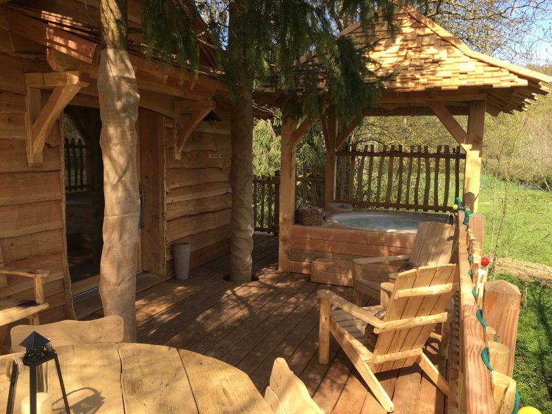 Cabane en bois avec terrasse, jacuzzi et mobilier en bois, au cœur de la nature.