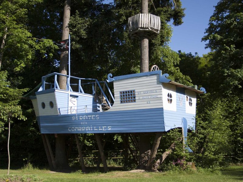 Cabane dans les arbres en forme de bateau pirate, entourée de verdure luxuriante.