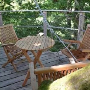 Cabane perchée dans les arbres avec terrasse en bois et chaises confortables.