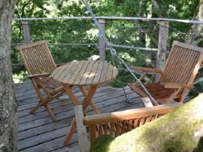 Cabane perchée dans les arbres avec terrasse en bois et chaises confortables.
