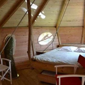 Cabane en bois avec lit douillet et fenêtre ronde, située en Pays de la Loire.