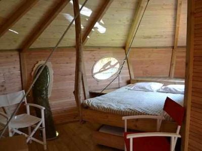 Cabane en bois avec lit douillet et fenêtre ronde, située en Pays de la Loire.