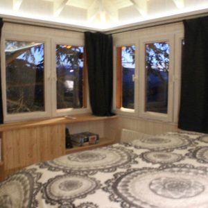 Cabane moderne en bois avec grandes fenêtres et lit douillet, vue sur la nature.