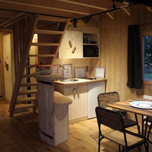Cabane en bois chaleureuse avec cuisine équipée et mezzanine, ambiance cosy.