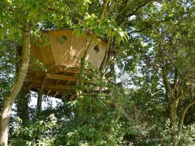 Cabane perchée dans les arbres, avec un cœur découpé dans le bois, entourée de verdure.