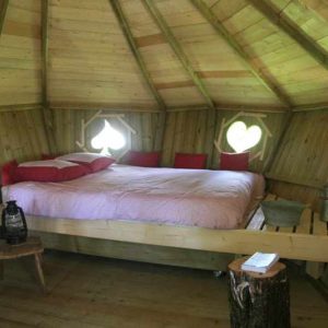 Cabane en bois avec lit douillet et fenêtres en forme de cœur, ambiance chaleureuse.