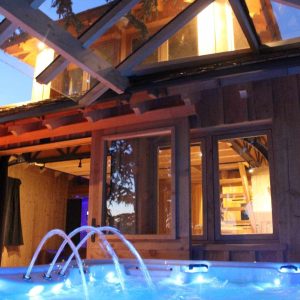 Cabane en bois avec jacuzzi, illuminée par des lumières douces au crépuscule.