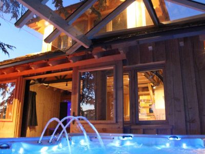 Cabane en bois avec jacuzzi, illuminée par des lumières douces au crépuscule.