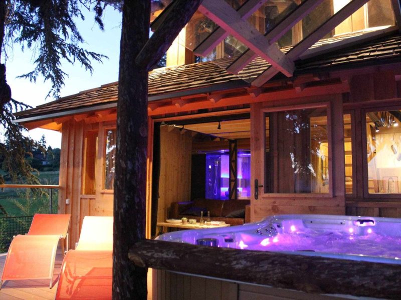 Cabane perchée en bois avec jacuzzi extérieur, ambiance lumineuse apaisante.