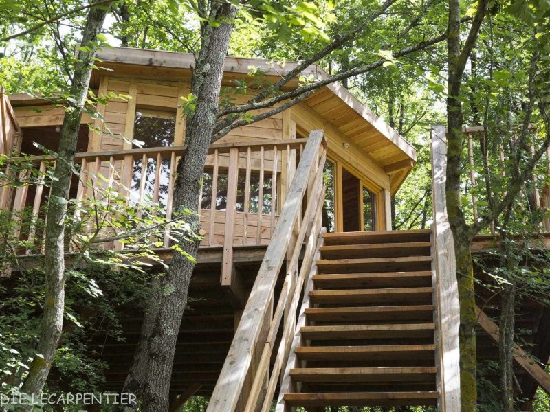 Cabane perchée en bois, entourée darbres, avec une terrasse en bois accueillante.