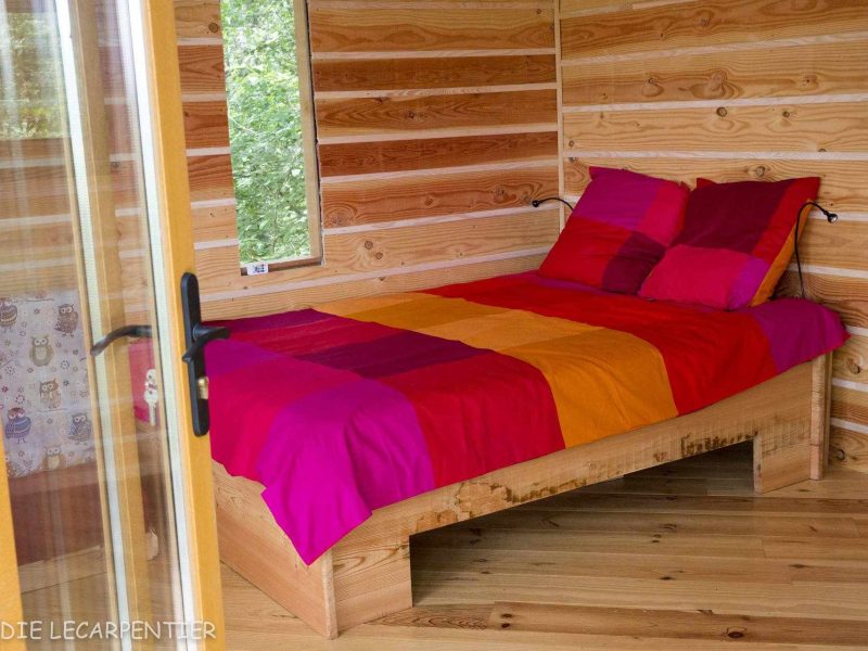 Chalet en bois avec un lit coloré aux draps vifs et un intérieur chaleureux.