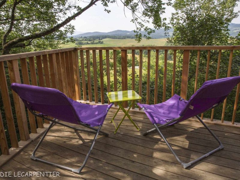 Chalet en bois avec chaises violettes et vue panoramique sur la nature environnante.