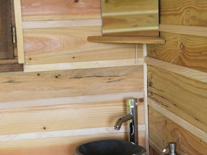 Salle de bain en bois dun hébergement en cabane, avec lavabo en pierre et miroir.